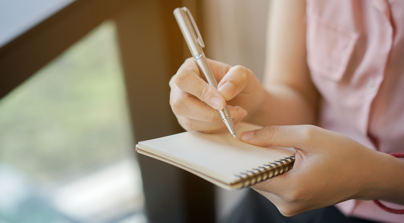 woman writing down information on a notepad