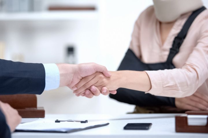 lawyer shaking hand of woman with a sling and neck brace