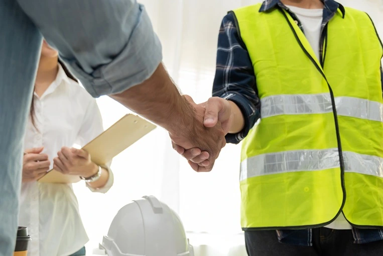 construction worker in a yellow vest shaking hands with his employer after reaching an agreement in a construction accident.